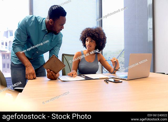Young multiracial male and female colleagues discussing over digital tablet in modern workplace