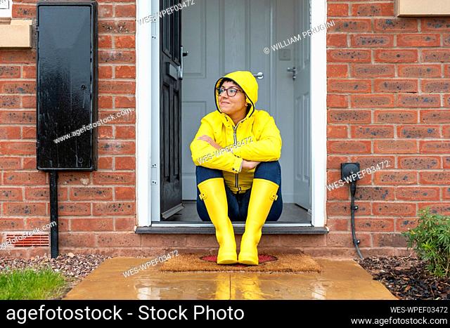 Woman looking away while sitting on doorway at home during rainy season