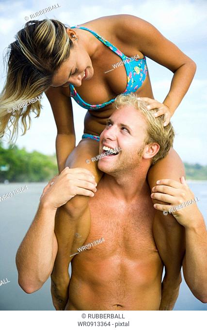 Close-up of a young man carrying a young woman on his shoulders and smiling