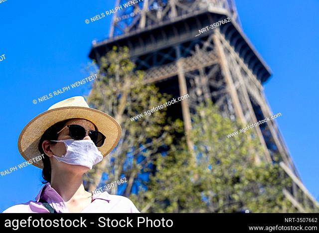 PARIS - An young French woman with a mouthmask to protect her against the coronavirus, in front of the Eiffel Tower. France will extend its nationwide lockdown...