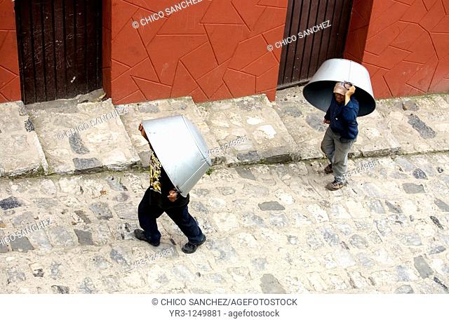 Men carry large metal pans for sale or barter in the Sunday market in Cuetzalan del Progreso, Mexico. Cuetzalan is a small picturesque market town nestled in...