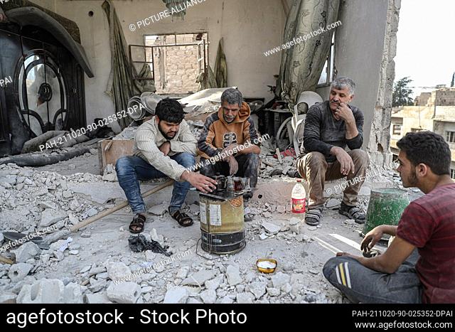 20 October 2021, Syria, Ariha: Khaled Ibrahim, 58, and his children sit for a cup of tea as they clean the rubble from their house