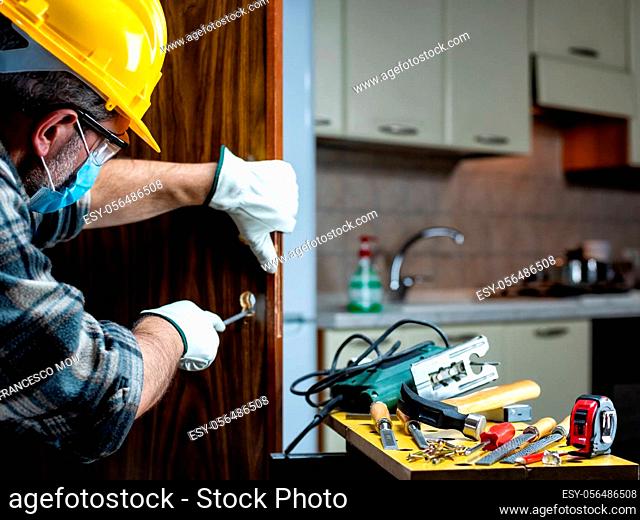 Carpenter worker at work repair and install a room door lock, wear the surgical mask to prevent Coronavirus infection. Preventing Pandemic Covid-19 at the...