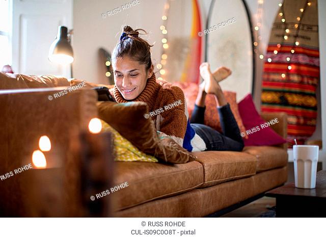 Young woman lying on living room sofa looking at laptop