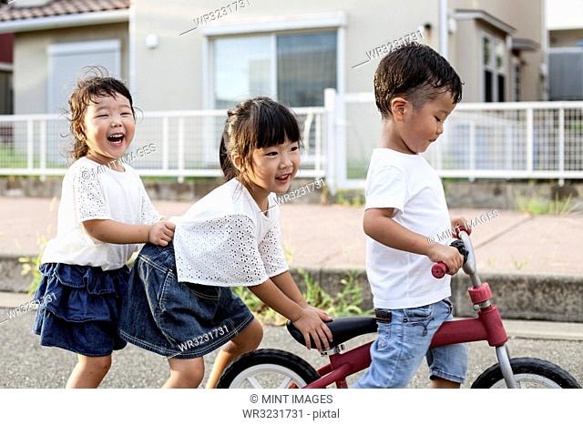 Portrait of two Japanese girls and boy playing on street with a bicycle, smiling at camera