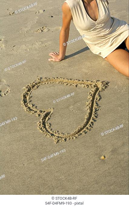 Woman sitting next to a heart drawn into the sand , high angle view