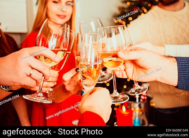New year or Christmas party at home, brothers and sisters cheering wishing all the best to each other. Close view of hands of young people clinking chamapgne...