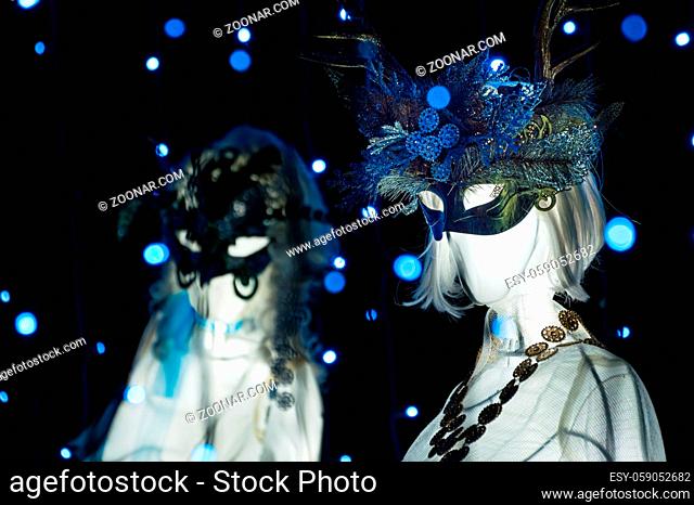 Masked white statues amongst blue fairy lights from the