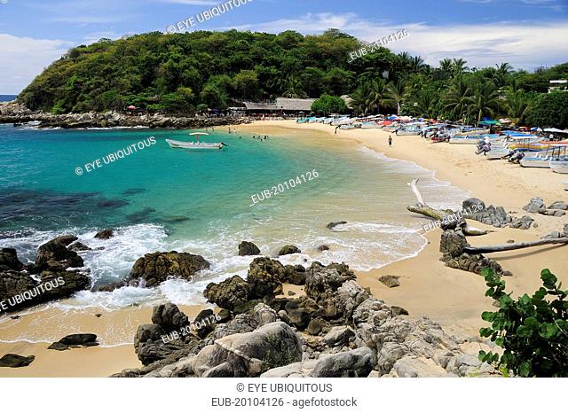View onto Playa Manzanillo beach with rocks and driftwood in foreground tourist boats people and tree covered headland beyond