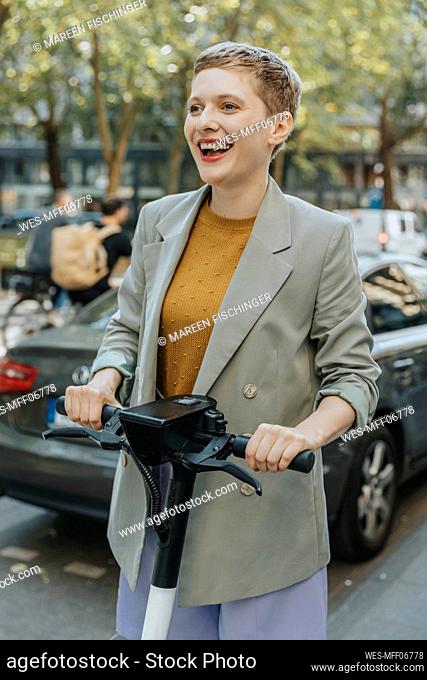Cheerful woman riding electric push scooter on street in city