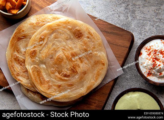 WELL COOKED PARANTHAS STACKED TOGETHER AND KEPT ON WOODEN TRAY WITH APPETIZERS