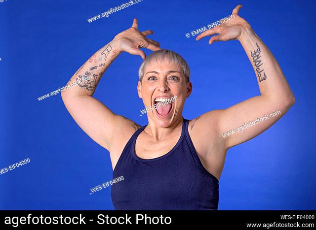Cheerful woman with arms raised standing against blue background