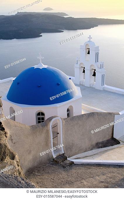 view of a typical church in White and Blue and the caldera at sunset on the island of Santorini Greece