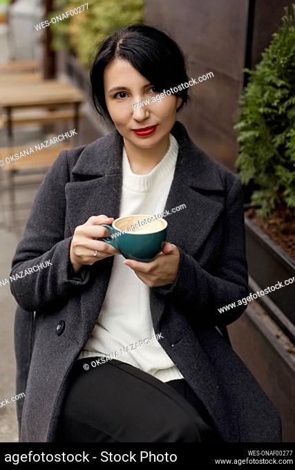 Beautiful woman holding coffee cup sitting at sidewalk cafe