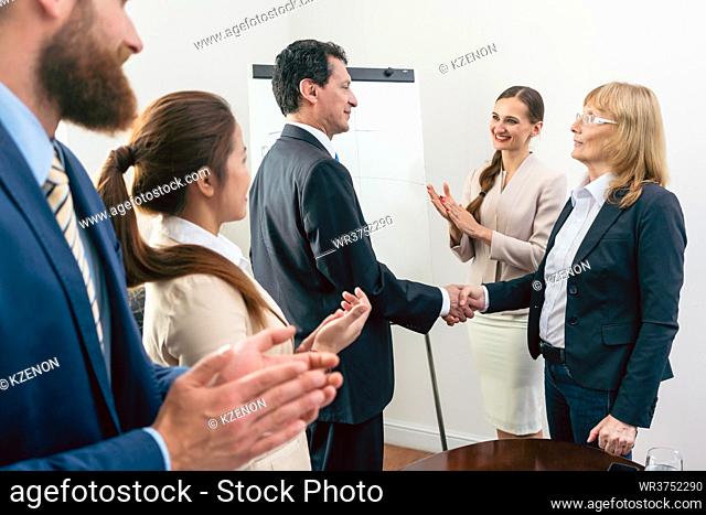 Two middle-aged business associates smiling while shaking hands as agreement after meeting in the conference room of a multinational company