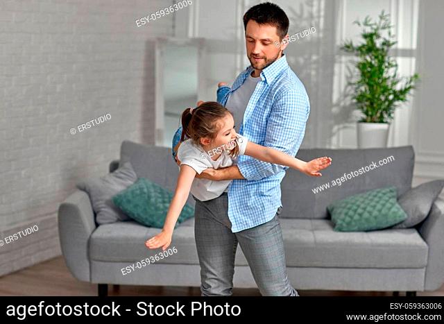 Happy little child girl flying in dads arms at home