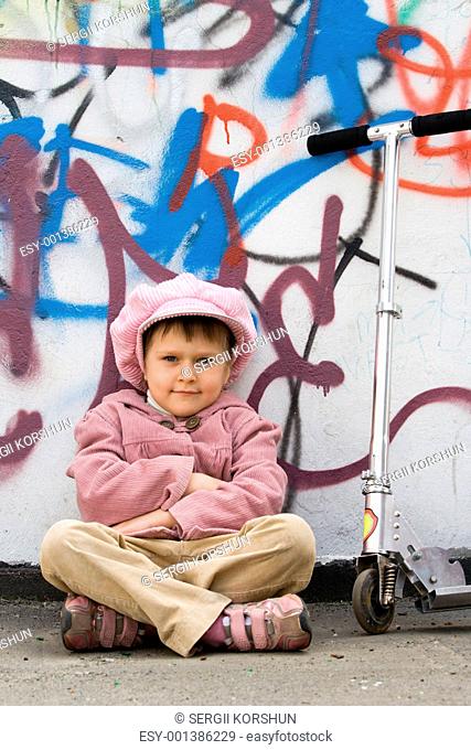 Funny little girl with scooter near graffiti painted wall