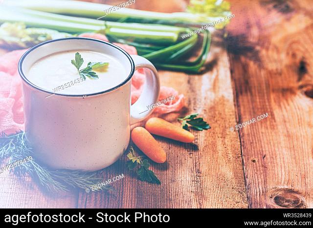 Vegetable soup puree with cheese in a white mug and vegetables on wooden background. Retro style filter