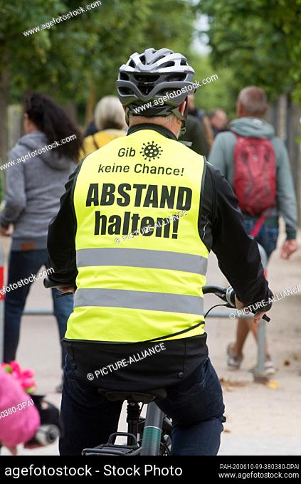 10 June 2020, Mecklenburg-Western Pomerania, Heringsdorf: A tourist wearing a safety vest with the inscription ""Keep your distance!"" drives along the beach...
