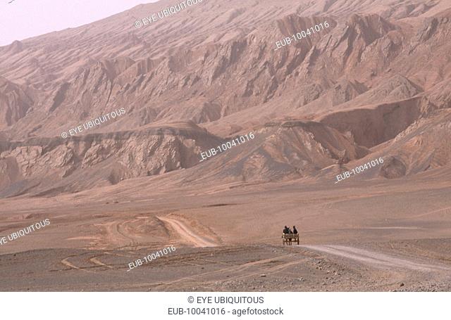 Desert landscape with horse drawn cart heading along dusty track
