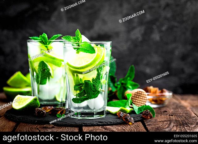 Refreshing mint cocktail mojito with rum and lime, cold drink or beverage with ice on black background