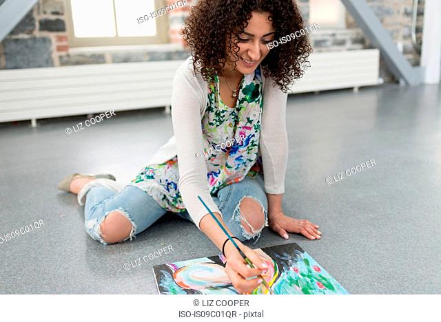 Young female painter painting canvas on studio floor