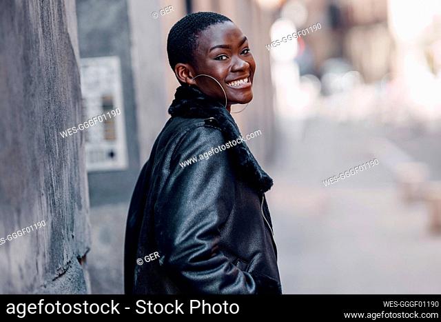 Happy woman wearing leather jacket by wall