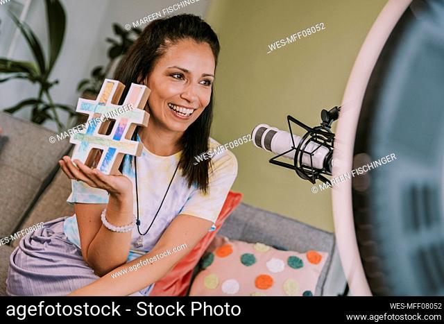 Smiling woman holding hashtag symbol while vlogging at home