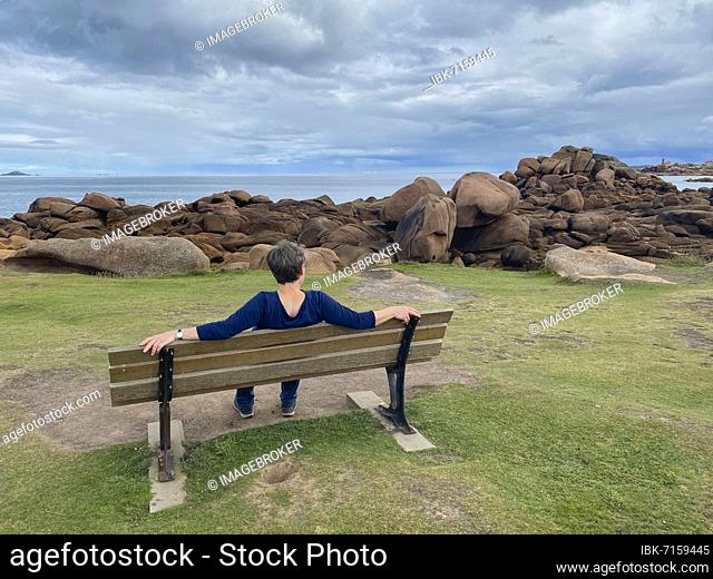 Elderly woman sitting on bench, Île Renote, rocky coast along the Sentier des douaniers, Trégastel, Côte de Granit Rose, Cotes d'Armor, Brittany, France, Europe