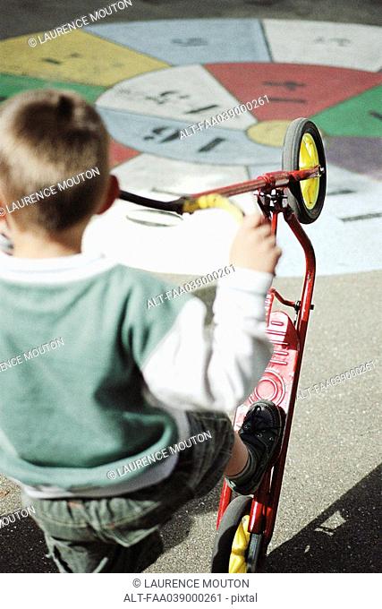 Boy playing with scooter on playground, rear view