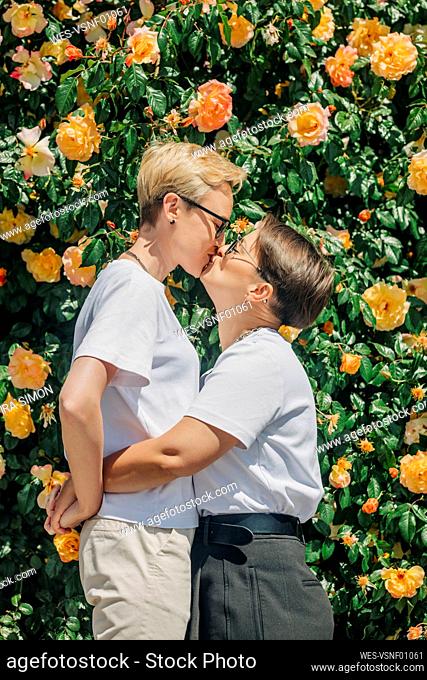 Lesbian couple kissing in front of wall with roses