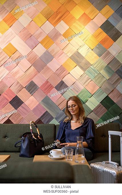 Portrait of businesswoman with baggage in a cafe looking at cell phone