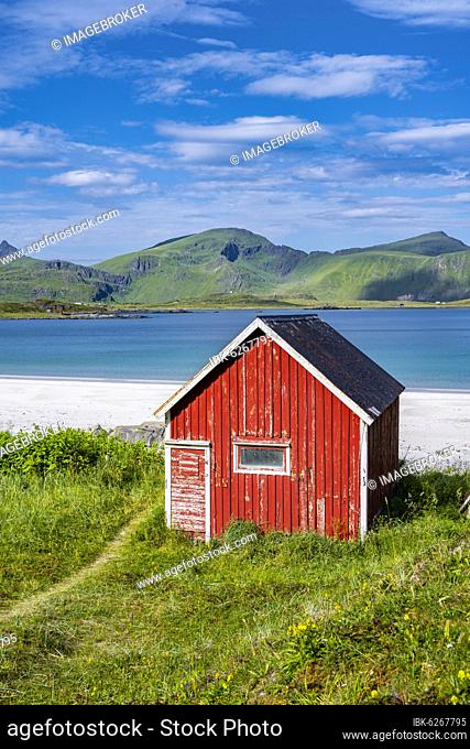 Rorbuer, traditional wooden house on sandy beach Rambergstranda, mountains and sea, Junesvika, Lofoten, Nordland, Norway, Europe