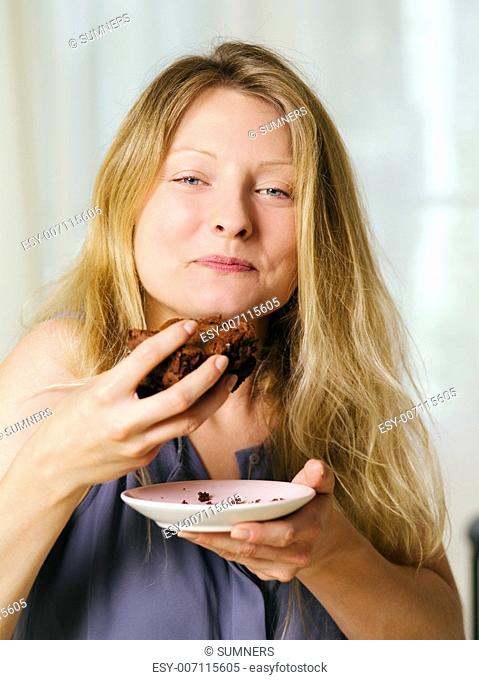 Photo of a beautiful blond woman in her early thirties with log blond hair eating a large piece of brownie or cake
