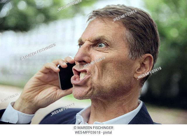 Portrait of angry mature businessman outdoors on the phone