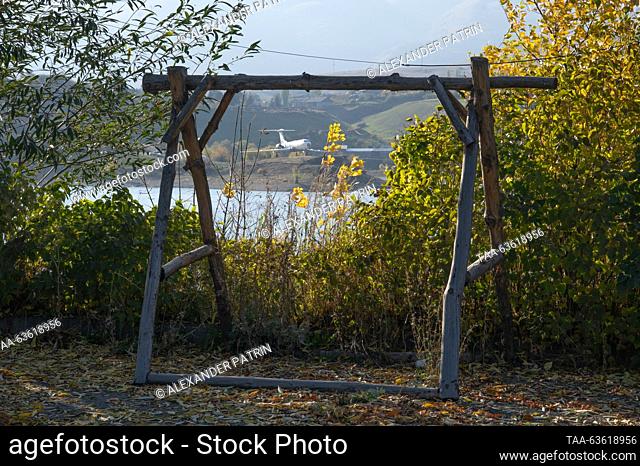 ARMENIA, KOTAYK PROVINCE - OCTOBER 21, 2023: A view of a wooden swing frame with an aircraft by a reservoir on the Hrazdan River in the distance, in autumn