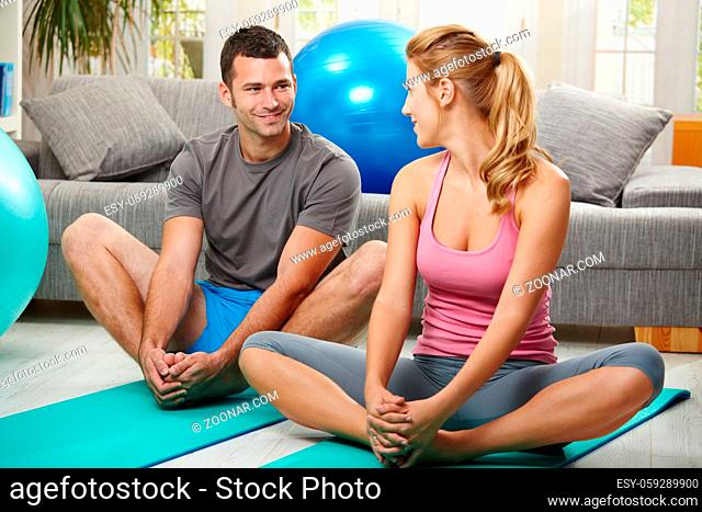 Young couple warming up before training, sitting on fitness mat, looking at each other smiling