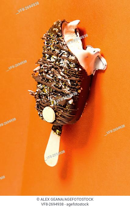 A chocolate bar isolotated on an orange background, drizled with toppings and more chocolate