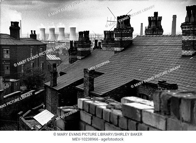 A view across the rooftops of terraced houses in Salford, Manchester toward the cooling towers of a large power station. Photograph by Shirley Baker