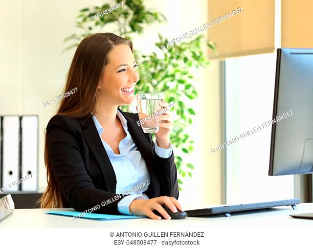 Happy businesswoman drinking water from a glass and looking through the window at office