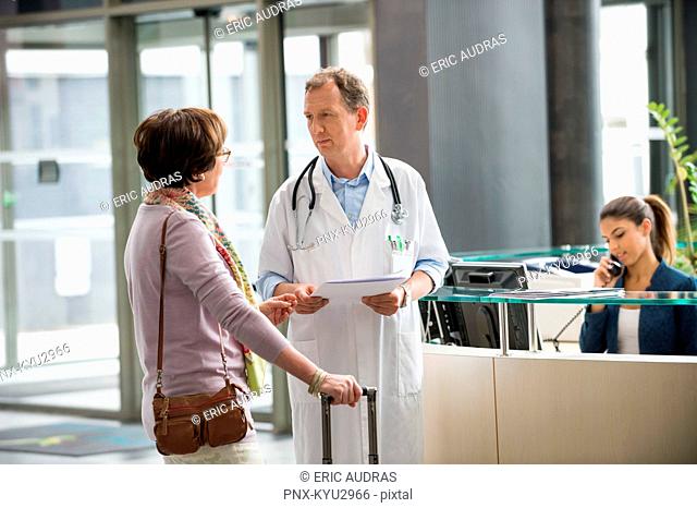 Male doctor discussing with his patient at hospital reception desk