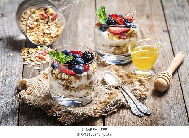 Homemade yogurt with baked granola and berries in small glasses on wooden background