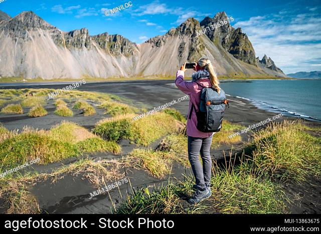Woman hiker with backpack at black sand dunes on the Stokksnes headland on southeastern Icelandic coast with Vestrahorn. Europe