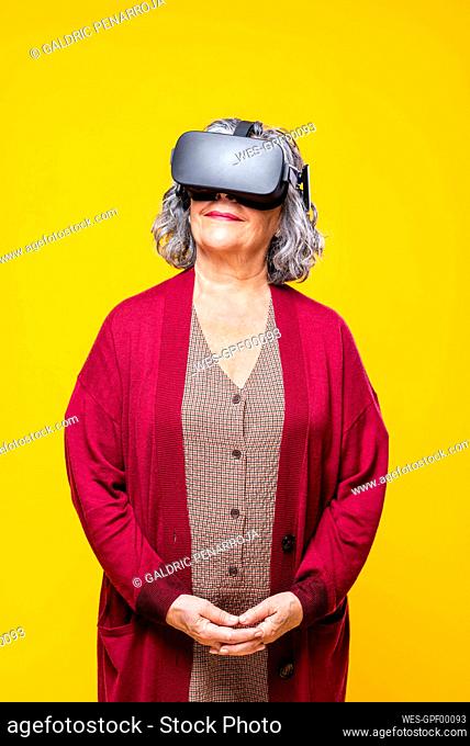 Smiling senior woman with virtual reality headset against yellow background