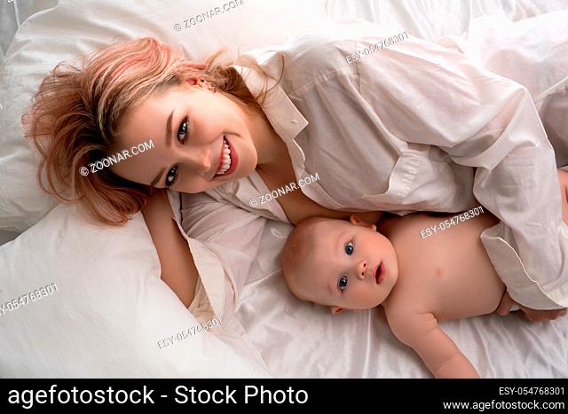 Baby boy and his mother lying in bed on white linen high angle view