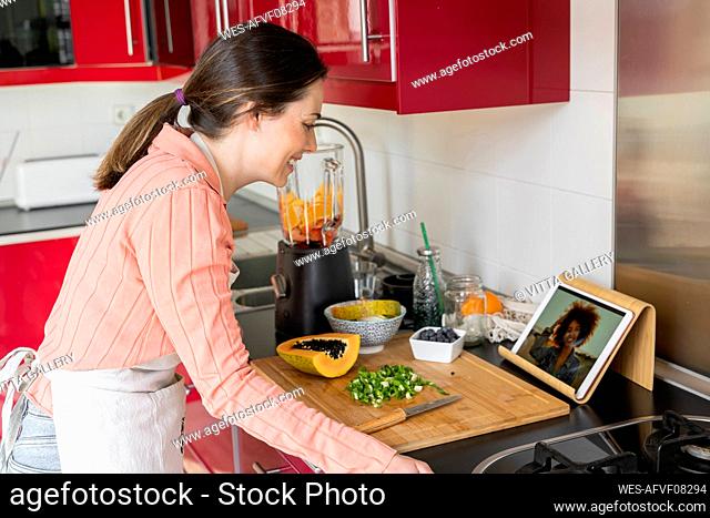 Young woman talking to friend through video call while standing in kitchen at home