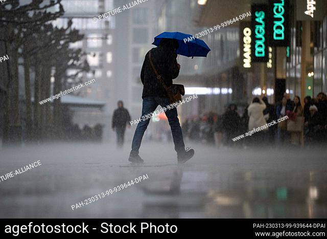 13 March 2023, Hesse, Frankfurt/Main: A man walks across the street during a heavy downpour on Frankfurt's Zeil shopping street