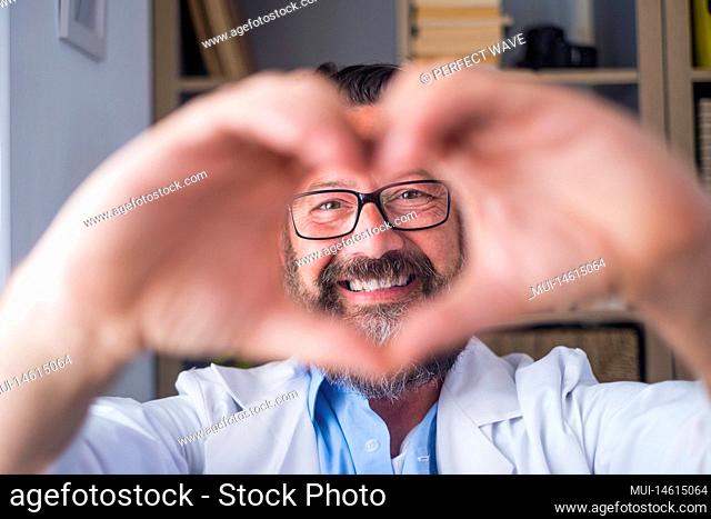 Man doing heart shape gesture with hands. Smiling handsome caucasian male doctor making a love symbol using his hands. Healthcare worker expressing love and...