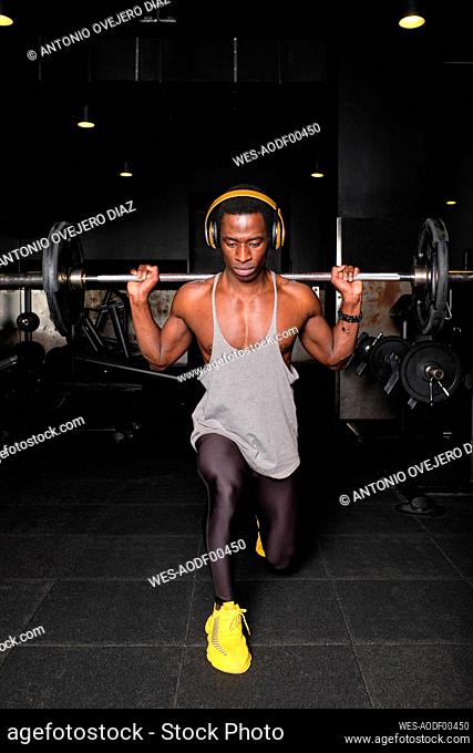 Muscular man with doing lifting barbell while doing lunge exercise at gym