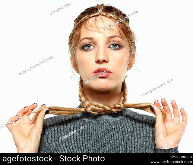 Portrait of beautiful young dark blonde woman. Female with creative braid hairdo on gray background. Girl holds braid ends in hands